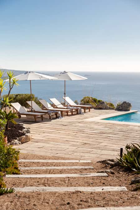 Stone terrace with an infinity pool and sun loungers offering panoramic sea views in Mallorca.